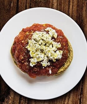 A plate of dakos salad featuring a base of barley rusk topped with tomato sauce and crumbled feta cheese. - Olive Oil Times