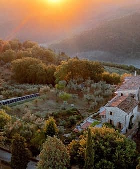 Aerial view of a rustic farmhouse surrounded by olive trees and hills during sunset. - Olive Oil Times