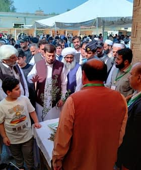 A group of people engaged in discussion at an outdoor event with a table displaying items. - Olive Oil Times