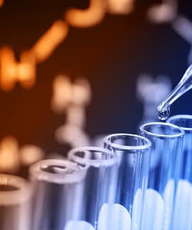 A pipette dropping liquid into a row of test tubes with a blurred clock in the background. - Olive Oil Times