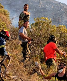 Firefighters and volunteers working together to manage a wildfire in a hilly area with vegetation. - Olive Oil Times