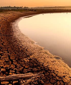 Dry, cracked earth along the edge of a river reflecting the sunset light. - Olive Oil Times