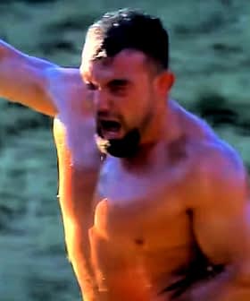 A shirtless man with a muscular build raising his arm in celebration outdoors. - Olive Oil Times