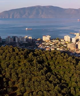 Aerial view of a coastal city with buildings and mountains in the background. - Olive Oil Times