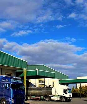 Dcoop warehouse building with two trucks parked in front under a blue sky. - Olive Oil Times