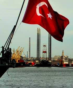 Turkish flag waving on a ship with cranes and industrial structures in the background. - Olive Oil Times
