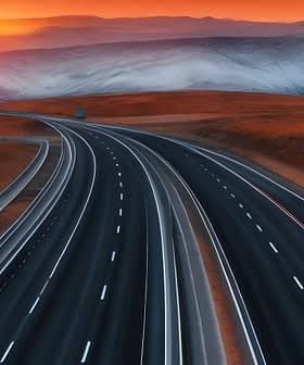 A highway winding through a mountainous landscape during sunset with orange and purple hues in the sky. - Olive Oil Times
