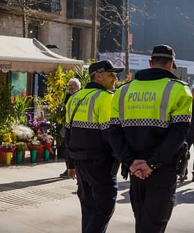 Two police officers in green and black uniforms walking in an urban area with a flower shop in the background. - Olive Oil Times