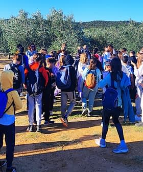 A large group of students gathered in an olive grove, wearing backpacks and casual clothing. - Olive Oil Times