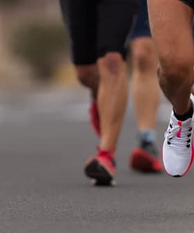 Close-up of a runner's foot in athletic shoes on a road with other runners in the background. - Olive Oil Times