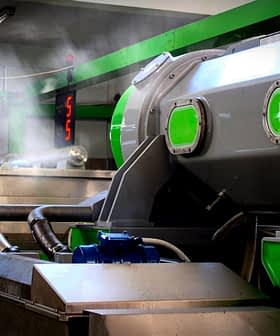 Industrial olive oil processing machine with green accents and steam emerging from the equipment. - Olive Oil Times