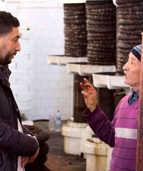 Two men talking inside an oil production facility, with equipment in the background. - Olive Oil Times