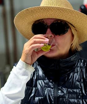 Woman wearing a straw hat and sunglasses tasting olive oil in a factory setting. - Olive Oil Times