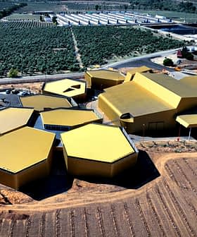 Aerial view of a modern olive oil processing facility with a hexagonal design and yellow roofs. - Olive Oil Times