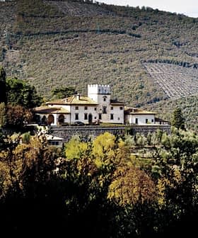 A villa with a tower situated on a hillside in Tuscany, surrounded by trees and rolling hills. - Olive Oil Times