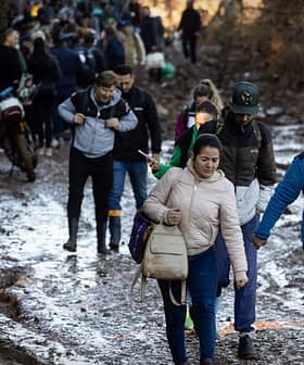 A group of people walking along a muddy path in a wooded area, some carrying bags. - Olive Oil Times