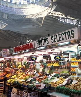 Market stall displaying a variety of fruits and vegetables under a large ceiling structure. - Olive Oil Times