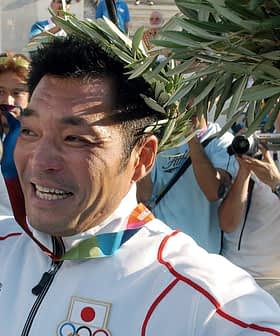 An athlete holding a medal and a laurel wreath while smiling at a crowd of photographers. - Olive Oil Times