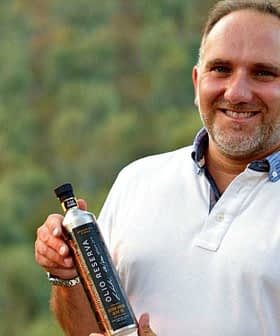 Man in a white polo shirt holding a bottle of olive oil with a blurred background. - Olive Oil Times