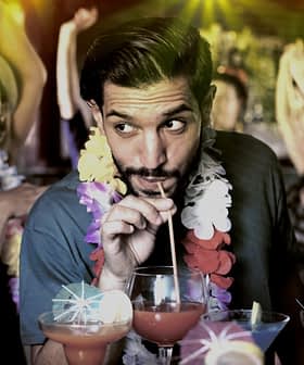 Man sipping a cocktail through a straw while surrounded by people at a party. - Olive Oil Times