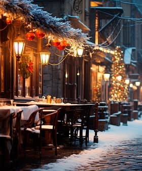 Outdoor dining area with tables and chairs on a snowy street during winter evening. - Olive Oil Times