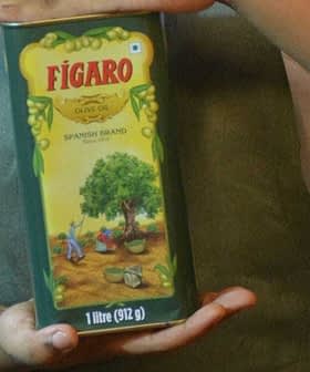 Persona che tiene in mano un contenitore di olio d'oliva verde della marca Figaro con l'illustrazione di un albero sull'etichetta. Olive Oil Times