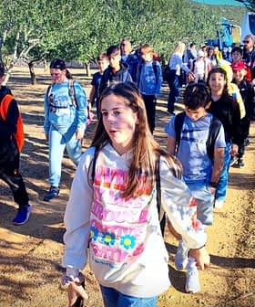 Um grupo de estudantes caminhando em um olival, usando mochilas e roupas casuais. - Olive Oil Times