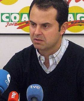 Moški, ki govori na tiskovni konferenci z več mikrofoni pred seboj. - Olive Oil Times