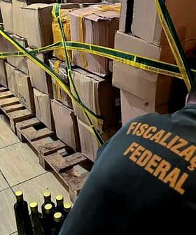 Škatle in steklenice, pritrjene z rumenim trakom v skladiščnem prostoru z osebo, ki jih pregleduje. - Olive Oil Times