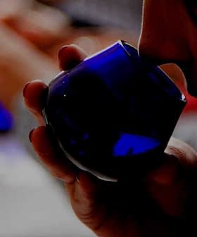 試飲中に青いガラス容器を持ち、オリーブオイルの匂いを嗅いでいる人。 - Olive Oil Times