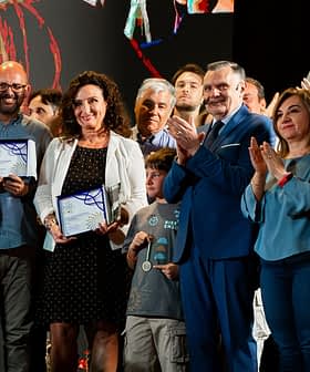Gruppo di persone a una cerimonia di premiazione, alcune con attestati in mano e applausi. - Olive Oil Times