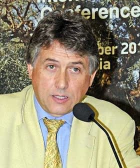 Un hombre con un traje de color claro habla por un micrófono en un evento de conferencia. Olive Oil Times