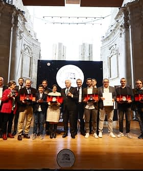 Gruppo di persone che tengono i premi sul palco durante una cerimonia in un edificio storico. - Olive Oil Times