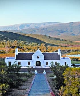 Edificio blanco de Galenia Estate con montañas y vegetación al fondo. - Olive Oil Times
