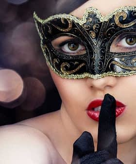 Frau mit schwarzer Maskerademaske und Finger auf den Lippen, die Ruhe signalisiert. - Olive Oil Times