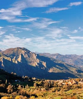 Mavi gökyüzünün altında vadide yer alan küçük bir köyün bulunduğu dağların manzarası. - Olive Oil Times