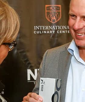 Un uomo sorridente mentre riceve un premio da una donna durante un evento culinario. - Olive Oil Times