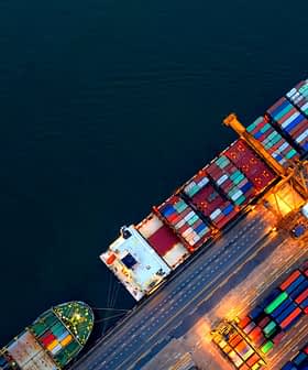 Luftaufnahme von Containerschiffen, die in einem Hafen anlegen, mit bunten Frachtcontainern, die auf dem Deck gestapelt sind. – Olive Oil Times