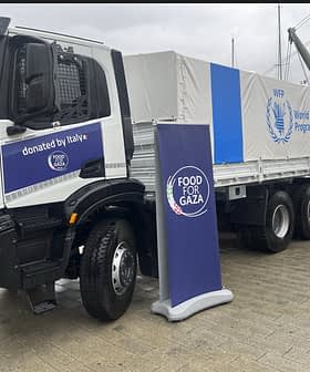 Camion Iveco con il marchio Mondo Food Programme, parcheggiato accanto a un cartello per l'iniziativa Food for Gaza. Olive Oil Times