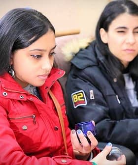 Дві молоді жінки сидять, одна в червоній куртці, інша в чорній куртці, кожна тримає синю чашку. - Olive Oil Times