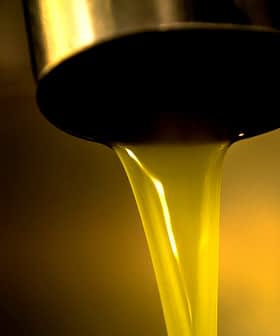 Azeite dourado fluindo de uma torneira de metal para um recipiente em uma visão de perto. - Olive Oil Times