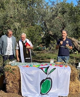 Quattro persone parlano durante un evento all'aperto con uno striscione a tema oliva davanti a loro. - Olive Oil Times