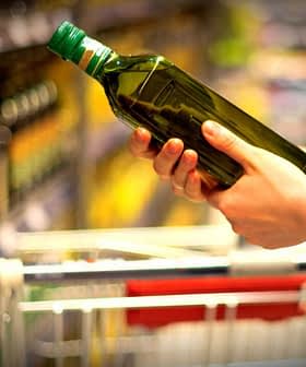 Posameznik drži zeleno steklenico oljčnega olja med nakupovanjem v trgovini z živili. - Olive Oil Times
