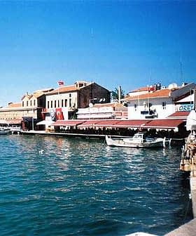 Blick auf ein Küstengebiet in Ayvalik mit Booten und Gebäuden entlang der Uferpromenade. – Olive Oil Times