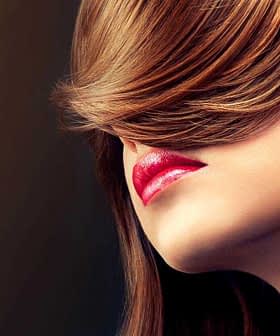 Vista de perfil de una mujer con cabello largo y castaño que cubre parte de su rostro y labios rojos. - Olive Oil Times