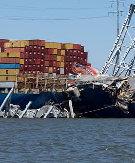 Nave cargo con container parzialmente sommersi e danneggiati, appoggiati a una struttura crollata. Olive Oil Times