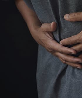Pojedinac nosi sivu košulju, drži se za trbuh objema rukama, što ukazuje na nelagodu. - Olive Oil Times