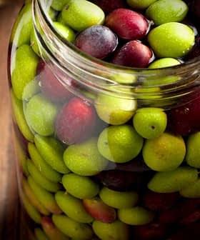 Tarro de cristal lleno de una mezcla de aceitunas verdes y negras sobre una superficie de madera. - Olive Oil Times