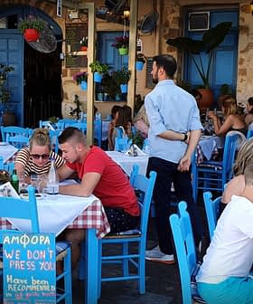 Jedilnica na prostem z mizami in modrimi stoli v restavraciji, kjer se gostje pogovarjajo. - Olive Oil Times