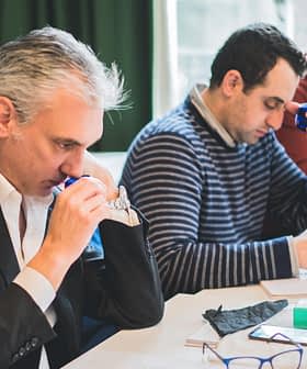 Três homens participando de uma sessão de degustação, concentrando-se em suas tarefas individuais e usando ferramentas de degustação. - Olive Oil Times